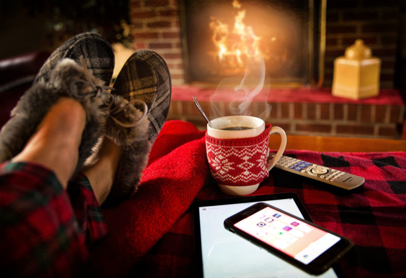 Person with slippers on with feet up in front of a fireplace with a mug of hot coco